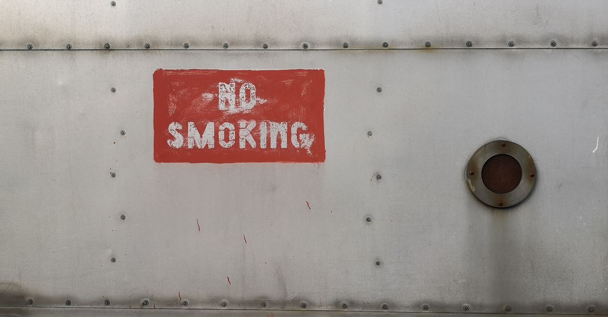 Close-up of a rusty 'No Smoking' sign painted on a metallic surface with rivets.